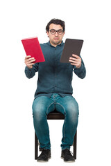 Pensive man student, seated on a chair looks confused, choosing between a traditional textbook and...