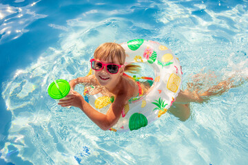 A little girl swims in an inflatable circle in the pool, with a cocktail in her hands