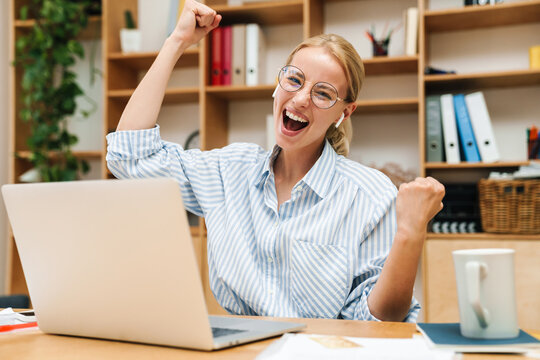 Image of woman using earphones and making winner gesture while working