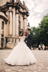 Stylish bride and groom gently hugging on european city street. Gorgeous wedding couple of newlyweds embracing near ancient building. romantic sensual moment of newlyweds
