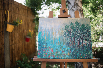 Painting on canvas placed on stand in garden. Tripod with watercolor drawing on canvas in backyard with flowers and plants.