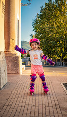 A little girl (child) learns to rollerblade on the street in the city. Safe with helmet and protections for elbows, wrists and knees. Concepts: fun, security, speed, balance, fear, danger.