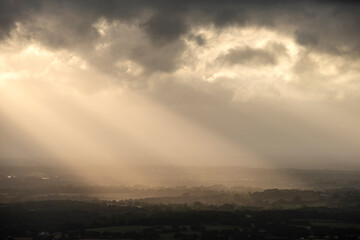 Beautiful landscape image of sunset over English countryside with sun beams lighting up the fields below