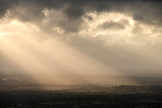 Beautiful landscape image of sunset over English countryside with sun beams lighting up the fields below