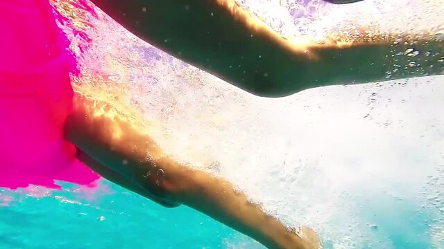 Slow motion footage of two girls swimming, holding on to a pink rubber mattress, underwater shot