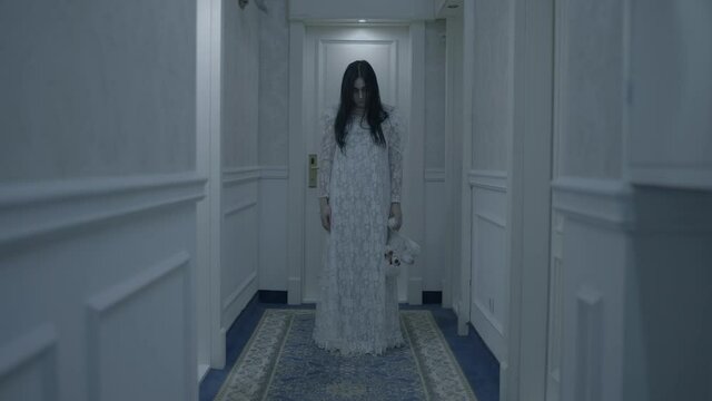 Mysterious female ghost in white gown dropping bloody toy on floor haunted house