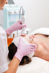 Obraz premium The cosmetologist makes the RF-lifting procedure for the client. View over the doctor's shoulder. Vertical. Concept of cosmetology and treatment