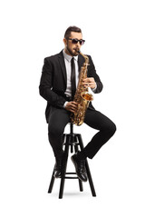 Handsome man in a black suit playing a saxophone and sitting on a chair