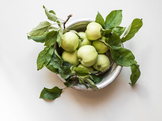 Metal bowl with green apples and leaves on a white background. Wallpaper of fruits.Top view, flat lay.