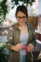 Pretty woman with glasses holding oil paint tube. Smiling female artist wearing glasses and opening red aquarelle paint tube outdoor.