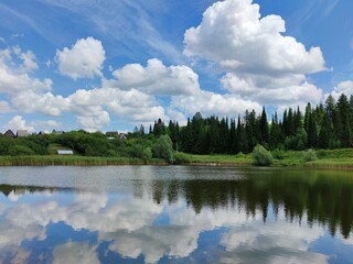 Fototapeta premium green shore of the lake near the village against the blue sky with clouds on a sunny day