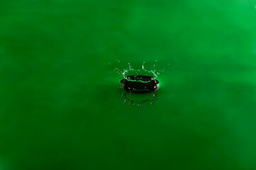 Drop green color falling and forming waves ripples