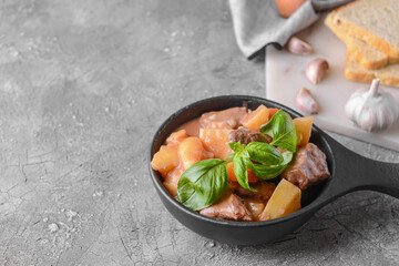 Frying pan with tasty beef stew on grey background