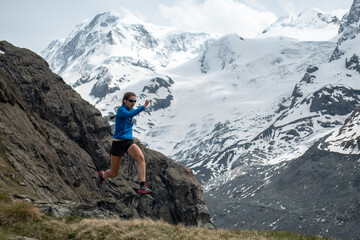 Trail runner woman jumping in alpine mountains with snow and glacier in the background
