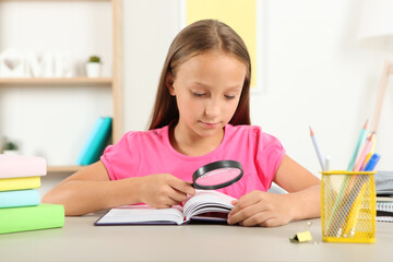 Cute little girl with poor eyesight reads with a magnifying glass
