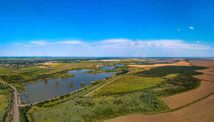 Obraz premium a small reservoir with four islands surrounded by wheat fields near the village of Lvovskaya (Krasnodar Territory, South of Russia) - aerial panorama view from a sunny summer day