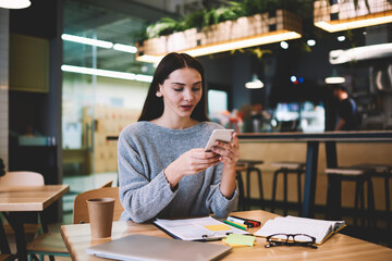 Attractive female owner of web store controlling work of content managers checking email box of online shop and rapid of answers to client requests using application on smartphone connected to wifi