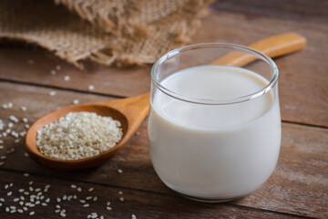 Sesame milk in glass and white sesame seeds on wooden spoon