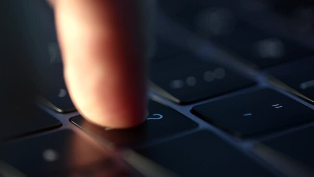 Finger constantly presses question button at night on backlit keyboard on laptop. Search for an answer on the web. People have a lot of questions. Cinematic footage of grey modern laptop