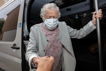 An elderly woman wearing a medical mask gets out of a disabled car.
the concept of transporting...