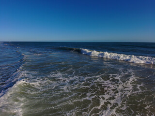 Fototapeta na wymiar waves breaking on the beach with deep green and blue ocean water and blue skies