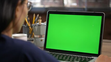 ​4K Dolly short. Over the shoulder shot of a business woman working in office interior on pc on desk, looking at green screen. Office person using laptop computer with laptop green screen, - Powered by Adobe