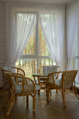 Rattan furniture on the summer porch. Outside the window is a pine forest