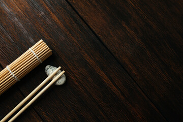 mat for rolls and chopsticks for chinese asian food on dark wooden background top view. Asian cutlery. With place for your text.