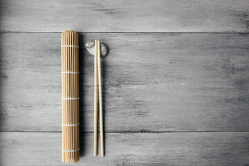 mat for rolls and chopsticks for chinese asian food on light wooden background top view. Asian cutlery.
