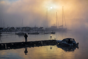 Early morning yacht dock in fog with fisherman silhouette - Powered by Adobe