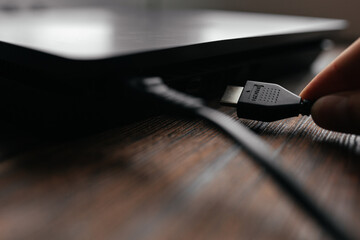 The man connects the HDMI cable to the device, inserting it into the HDMI port. Different interfaces connecting devices with each other.