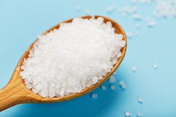 In a wooden spoon, sea salt crystals on a blue background, macro.