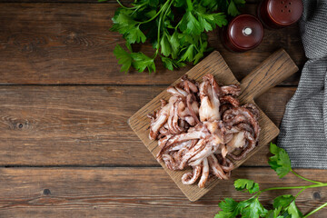 The tentacles of squid. Raw squid tentacles on a wooden serving Board on a brown wooden kitchen table. Lots of squid tentacles. The view from the top	