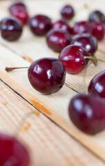 Red ripe cherries with tails on a wooden background. The side view is randomly placed on the table. Vertical orientation