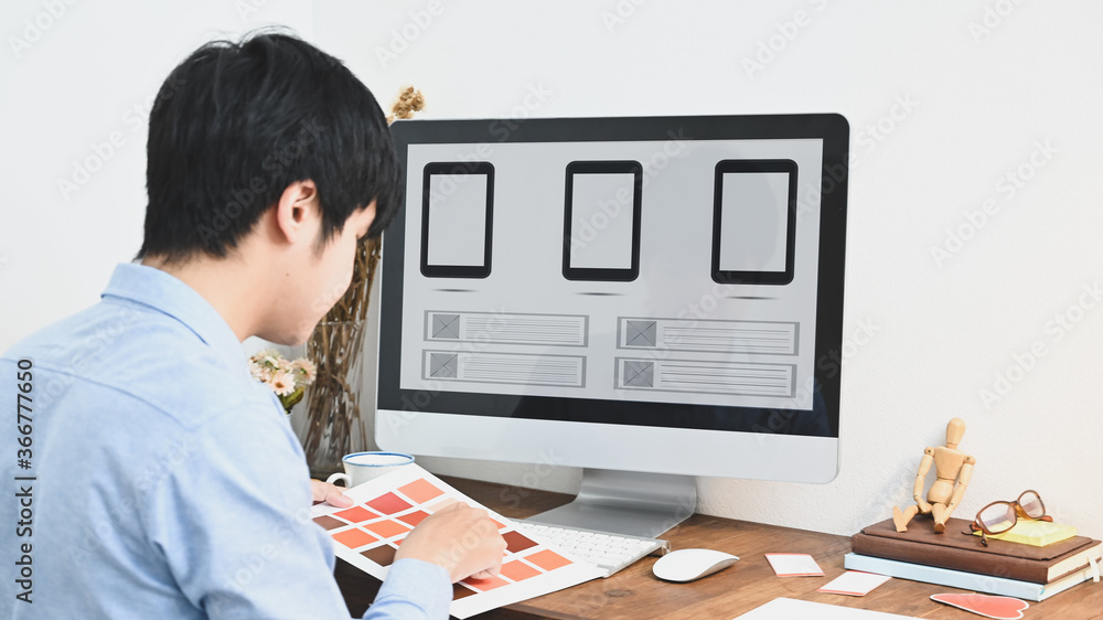 Aufkleber a graphic designer is selecting a color while sitting in front of a computer at the wooden table.
