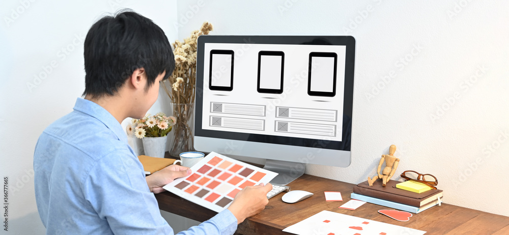 Aufkleber a graphic designer is selecting a color while sitting in front of a computer at the wooden table.