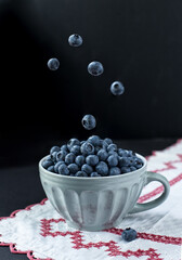 A cup o fresh tasty blueberries, some of them in the air.