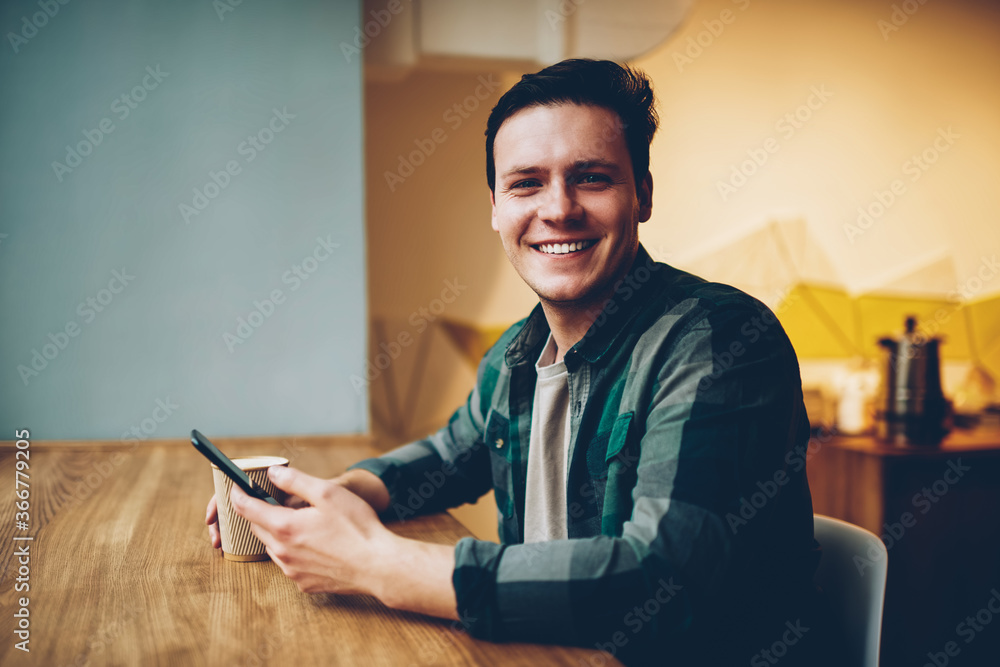Poster portrait of cheerful hipster guy in casual wear enjoying coffee break chatting via telephone, happy 