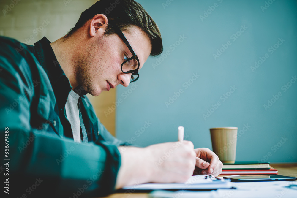 Poster close up view of smart student in spectacles writing essay for homework task concentrated on learnin