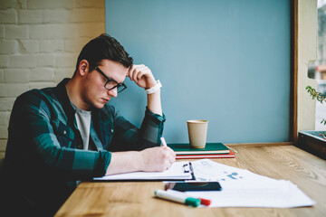 Contemplative smart student solving problem for homework task concentrated on learning, clever hipster guy creating plan for coursework project analyzing information and accountings in papers