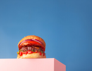 Fresh juicy beef hamburger placed on the stand and blue background. Copy space for text, trendy...