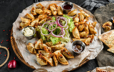 Assorted snacks for beer in plates, roasted chips, bbq sauce, onions and beer in glass on dark background, top view