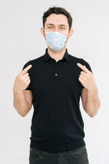 Caucasian young man with protecting from the coronavirus with medical mask over white isolated background pointing to the face and mask. Prevention of virus infection, Coronavirus COVID-19.