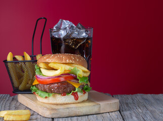 Fresh juicy beef hamburger with french fries and cola placed on wooden background