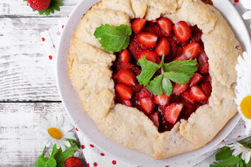 Shortbread galette with strawberry surrounded by berries and chamomiles on the white wooden table. Top view