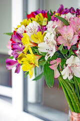Alstroemeria bouquet of flowers in a vase by the window. Beautiful bouquet of colorful flowers in the apartment by the window.