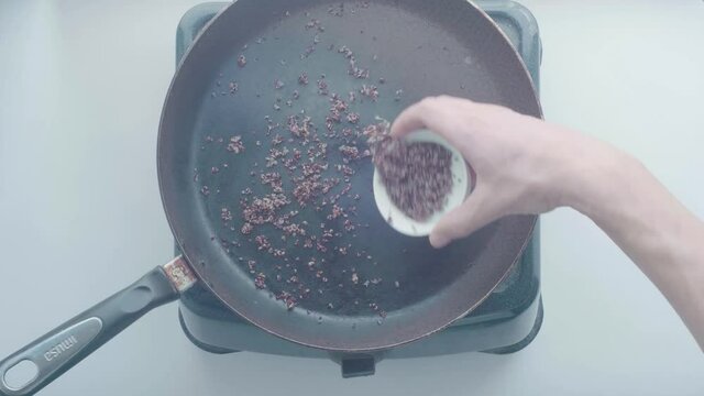 White Man's Hand Puts Quinoa on a Black Frying Pan 