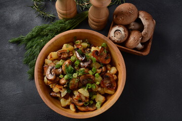 Fried potatoes with mushrooms in a wooden bowl. Rustic style.