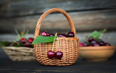 Fototapeta na wymiar cherries in a basket in a wicker plate and bowl on a dark wooden background close up