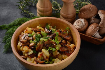 Fried potatoes with mushrooms in a wooden bowl. Rustic style.